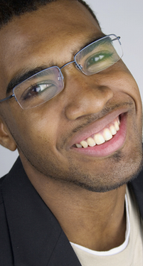 Smiling man wearing glasses and dark blazer against neutral background, professional headshot.