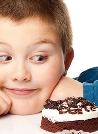 Young boy gazing at chocolate cake slice with eager expression on white background.