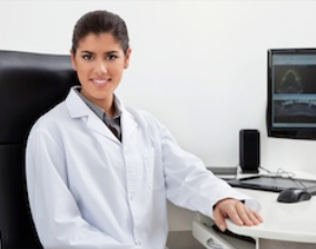 Female healthcare professional in white coat at desk in medical office with computer monitor