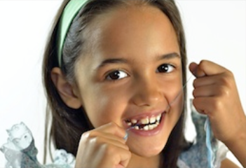 Young girl smiling at camera while flossing teeth against white background.