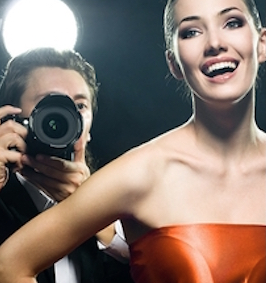 Photographer with camera and woman in orange dress posing under studio lighting