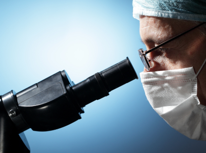 Scientist wearing protective gear examines specimen through microscope against blue background.