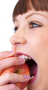 Woman with bangs biting into a fresh apple against white background.