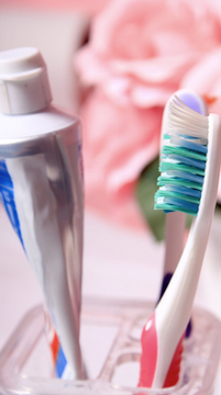 Colorful toothbrushes in holder with pink towel and toiletries in bathroom setting.