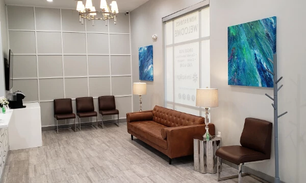 Modern medical waiting room with brown leather seating, large windows, and contemporary artwork on walls.