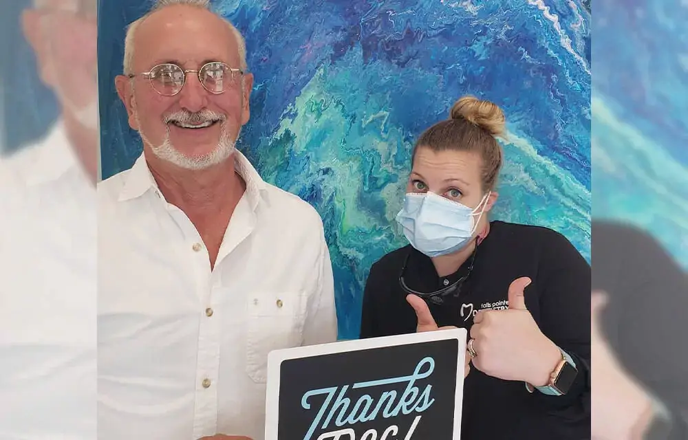 Two people hold a "Thanks" sign in front of a blue ocean backdrop at Falls Pointe event.