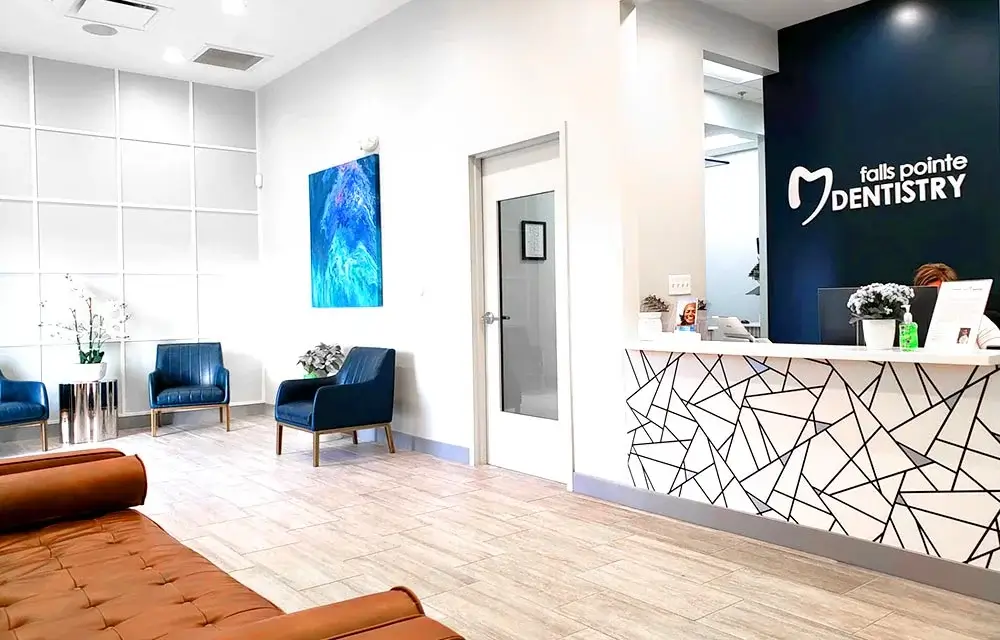 Modern dental office waiting room with blue chairs, geometric reception desk, and contemporary decor.