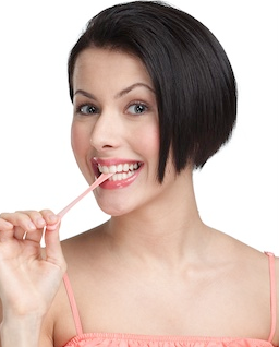 Woman with short dark hair smiling while holding pink toothbrush against white background.