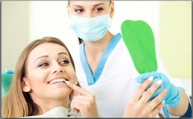 Dentist in mask showing green shade sample to smiling female patient in dental office.