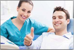 Healthcare professional in blue scrubs giving thumbs up with smiling male patient in clinical setting.