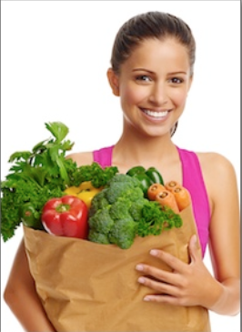 Woman in pink tank top holding paper bag filled with fresh vegetables and produce.