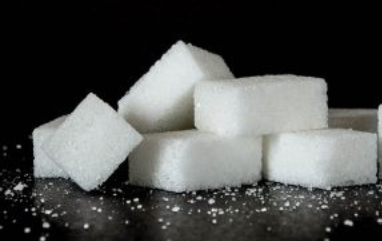 White sugar cubes stacked on dark surface with scattered granules.