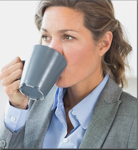 Professional woman in business attire drinking from gray mug at office.