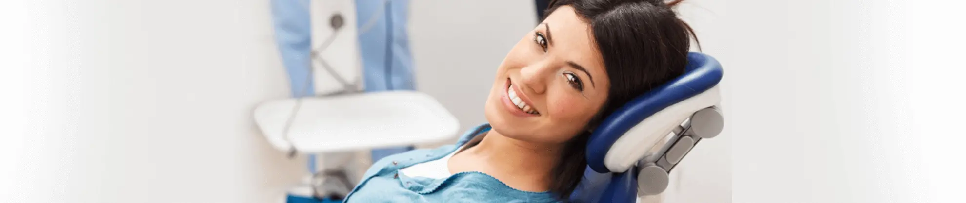 Woman in dental chair wearing blue bib, smiling during dental examination or treatment.