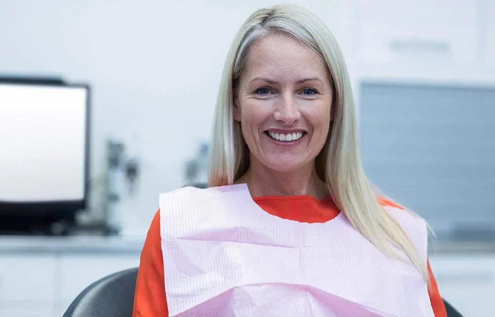 Woman with blonde hair smiling in modern office setting wearing red and white top.