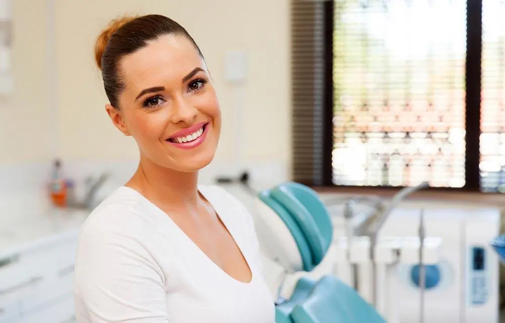 Female dental professional smiling at camera in modern dental office treatment room.
