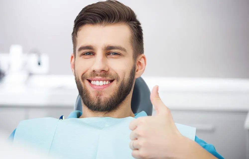 Smiling man giving thumbs up in dental office wearing blue bib