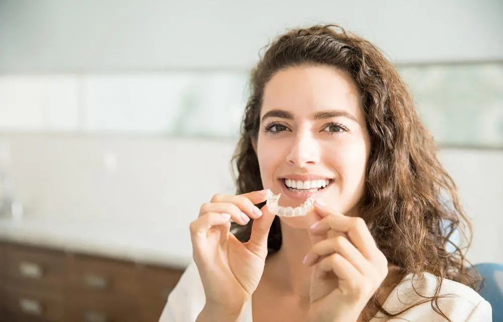 Woman holding dental floss and smiling in a bright, modern bathroom setting.