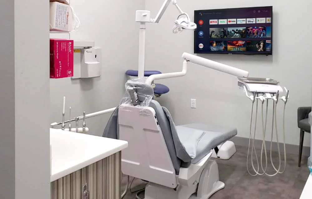 Modern dental operatory with chair, overhead light, equipment, and monitor at Falls Pointe dental office.