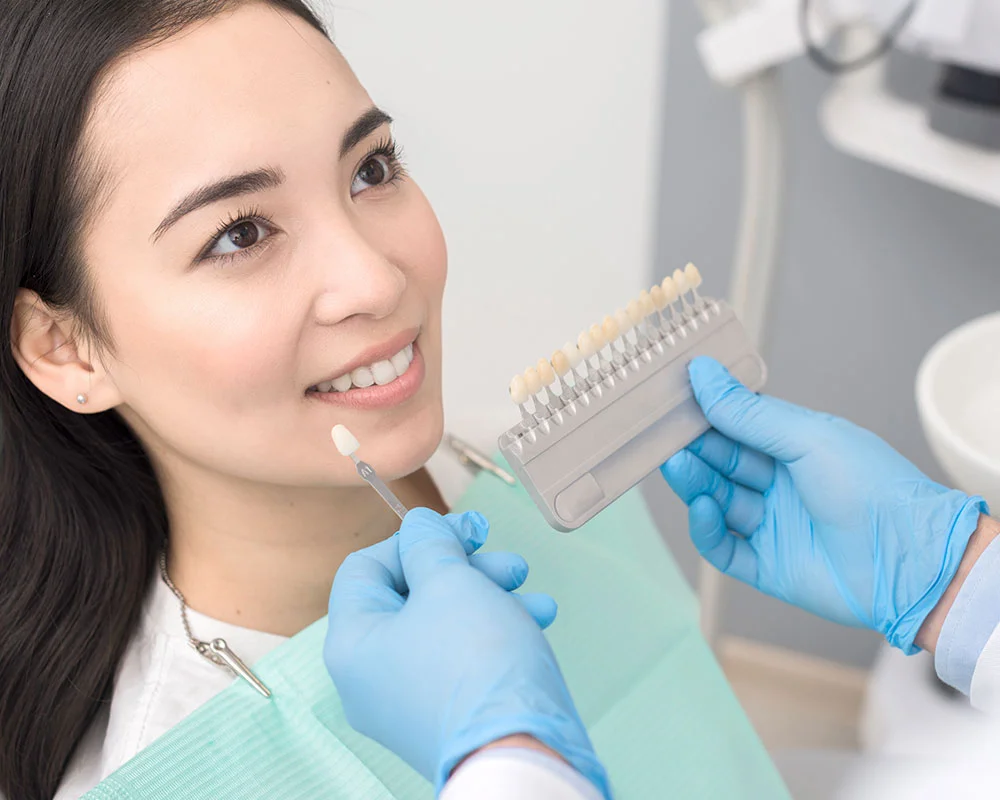 Dental hygienist in blue gloves holds shade guide during patient consultation in modern dental office.