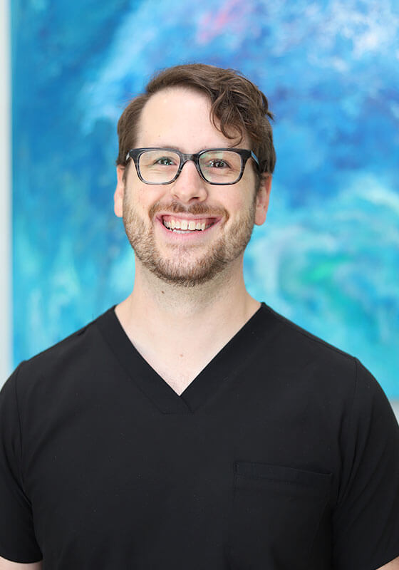 Man wearing glasses and black shirt smiling at camera against blue abstract background.