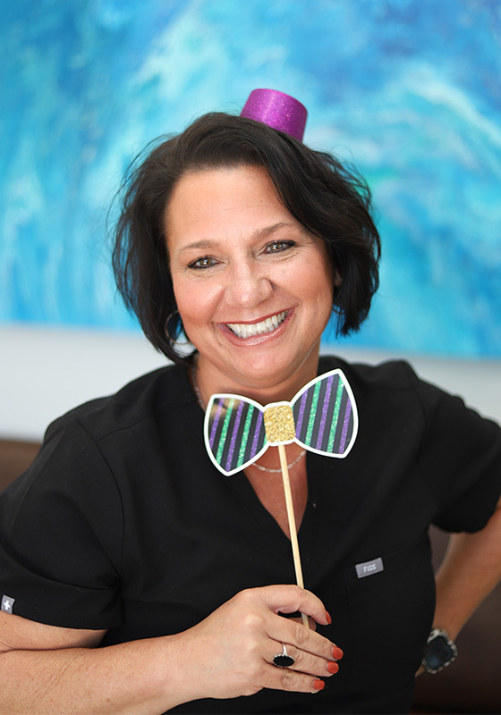 Smiling woman holding decorative bow tie prop against blue water background at Falls Pointe.