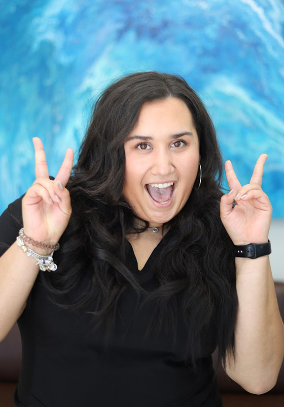 Woman making peace signs and smiling against blue water background at Falls Pointe.